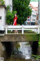 A woman in a red dress standing on a bridge over a stream.