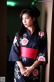 A woman in a black and pink kimono leaning against a wall.